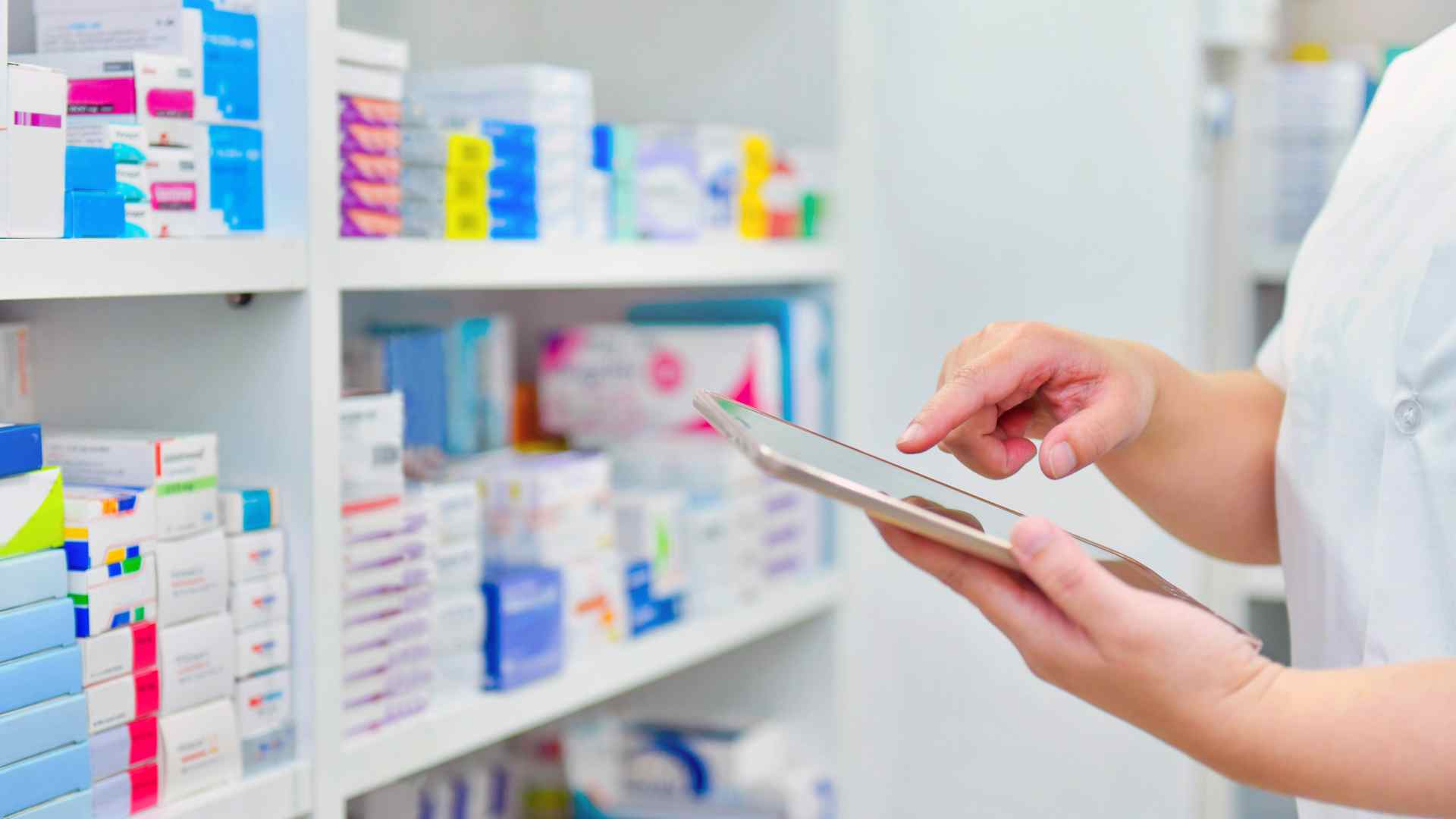 Pharmacist using a tablet beside shelves of medicine