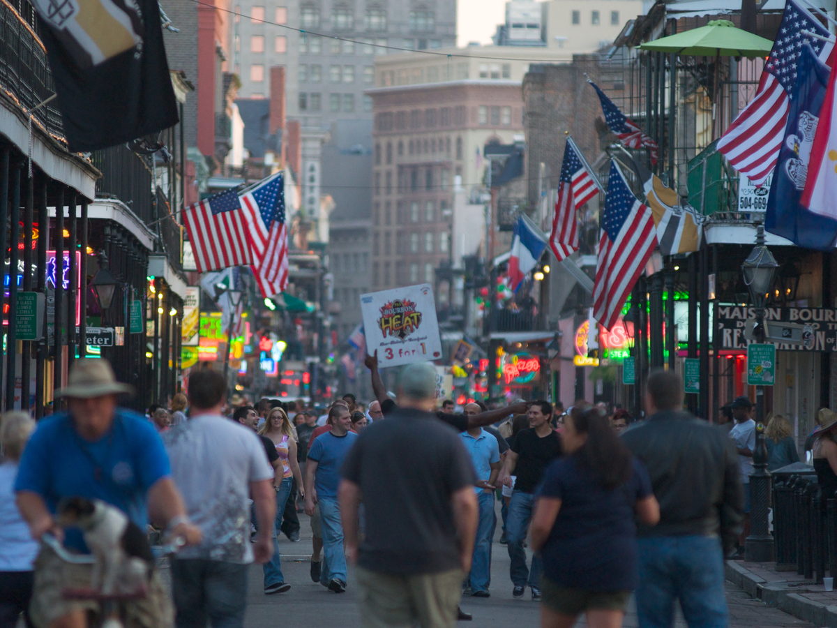 Crowds walking beneath signs and flags on Bourbon Street in New Orleans