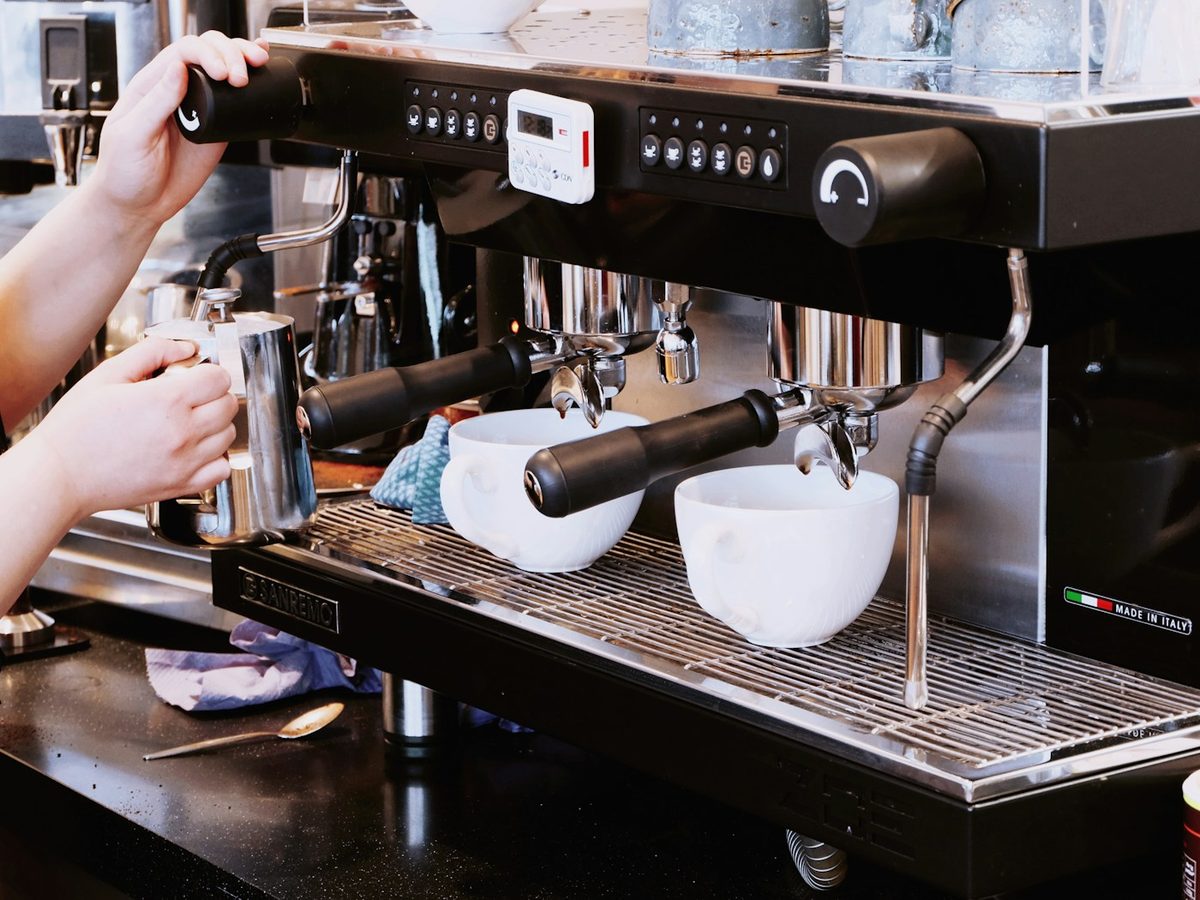 Barista steaming milk beside a commercial espresso machine