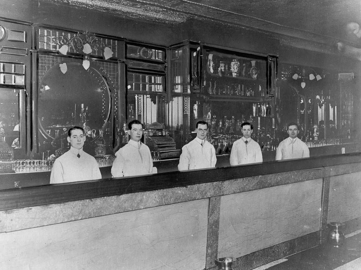 Bartenders standing behind a historic bar counter