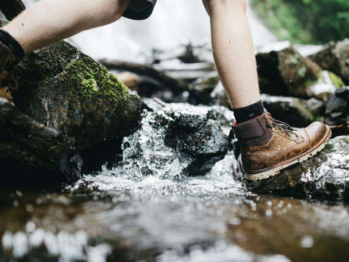 Brown hiking boot stepping across a rocky stream
