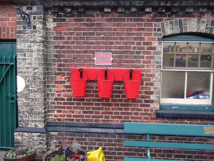 Three red metal fire buckets hanging at a station