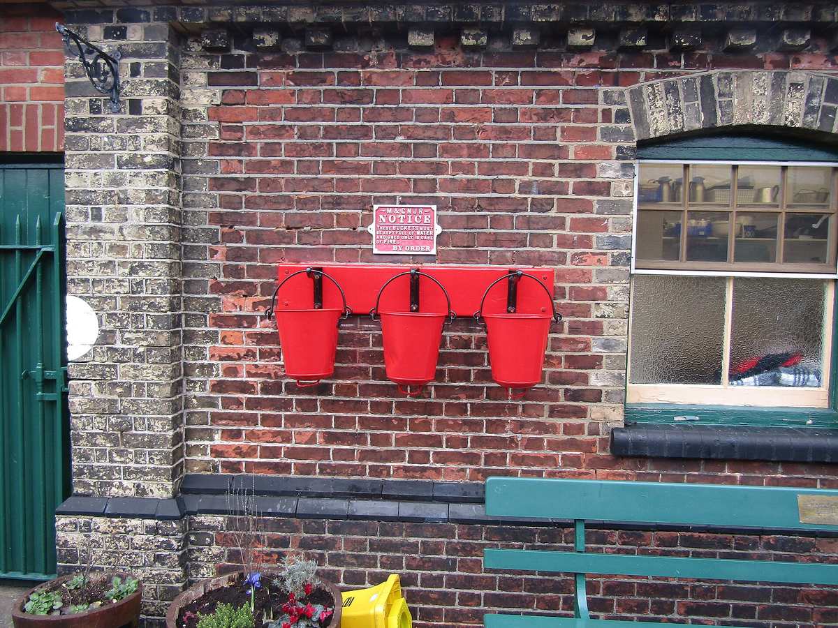 Three red metal fire buckets hanging at a station