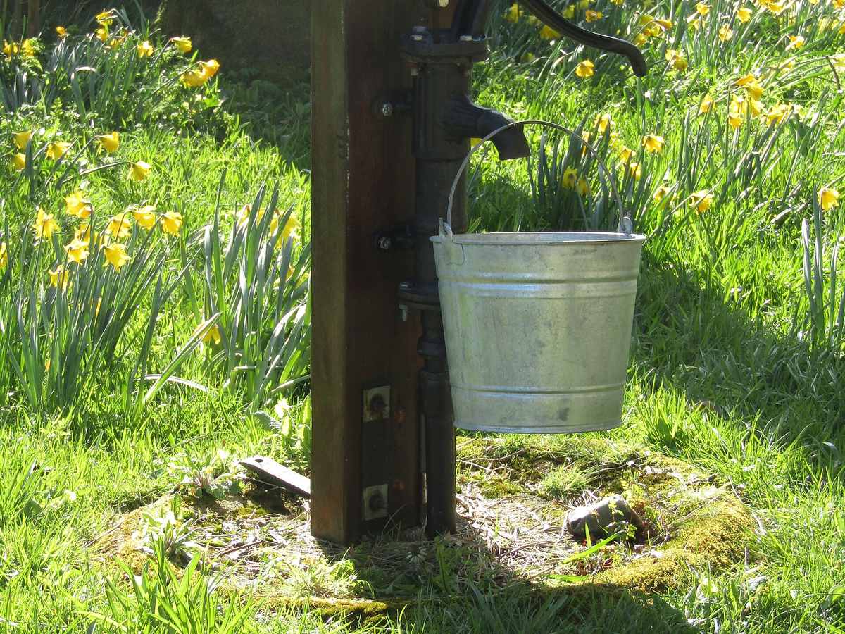 Metal bucket beside an old-fashioned hand water pump