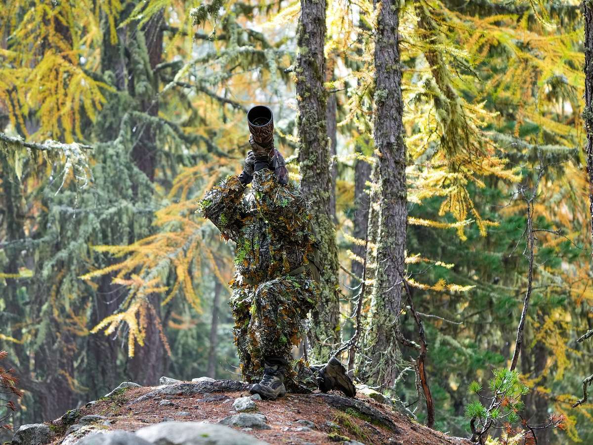 Photographer in camouflage clothing using a camera in nature