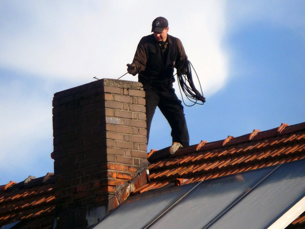 Chimney sweep carrying coiled cleaning rods beside a rooftop chimney