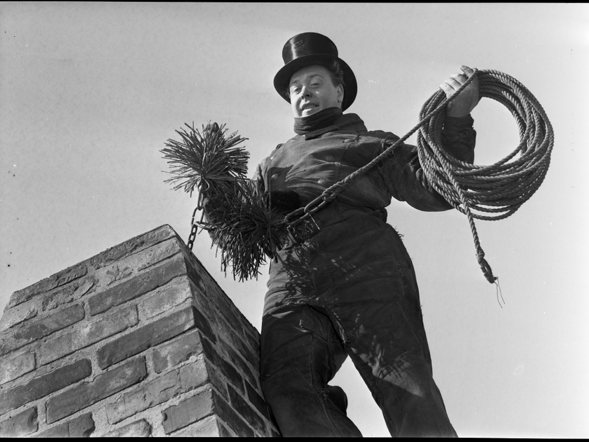 Chimney sweep holding a flue brush while standing on a brick chimney