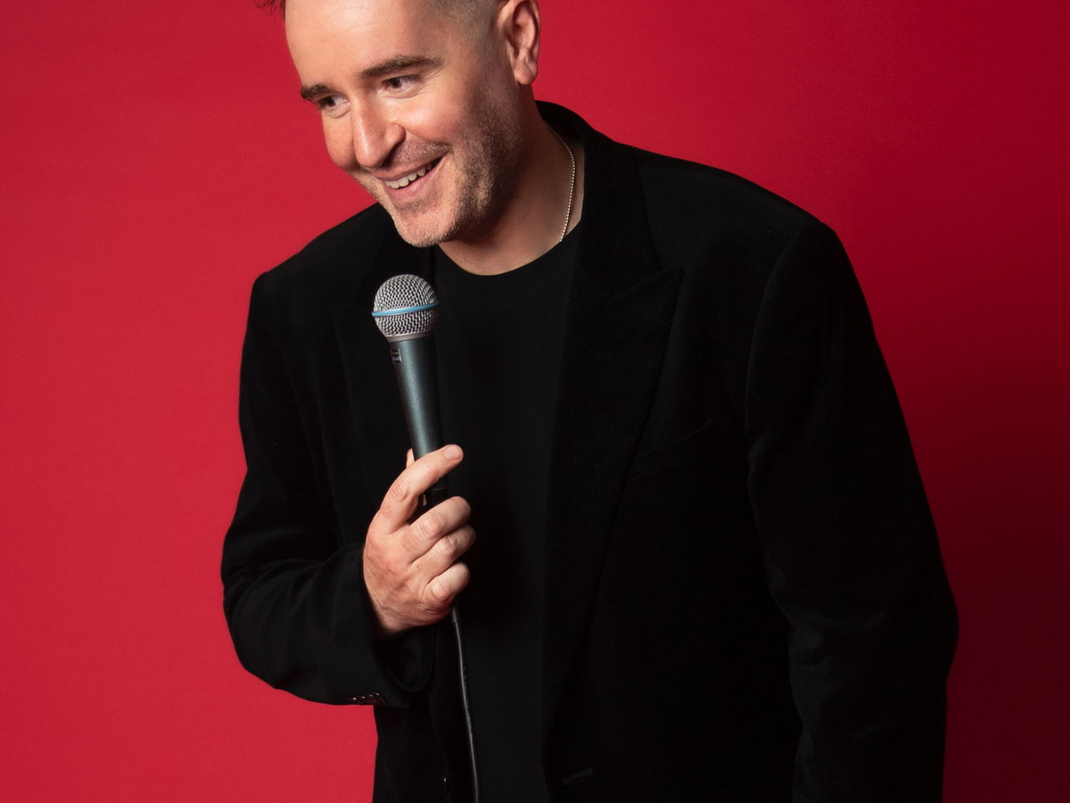 Stand-up comedian smiling while holding a microphone