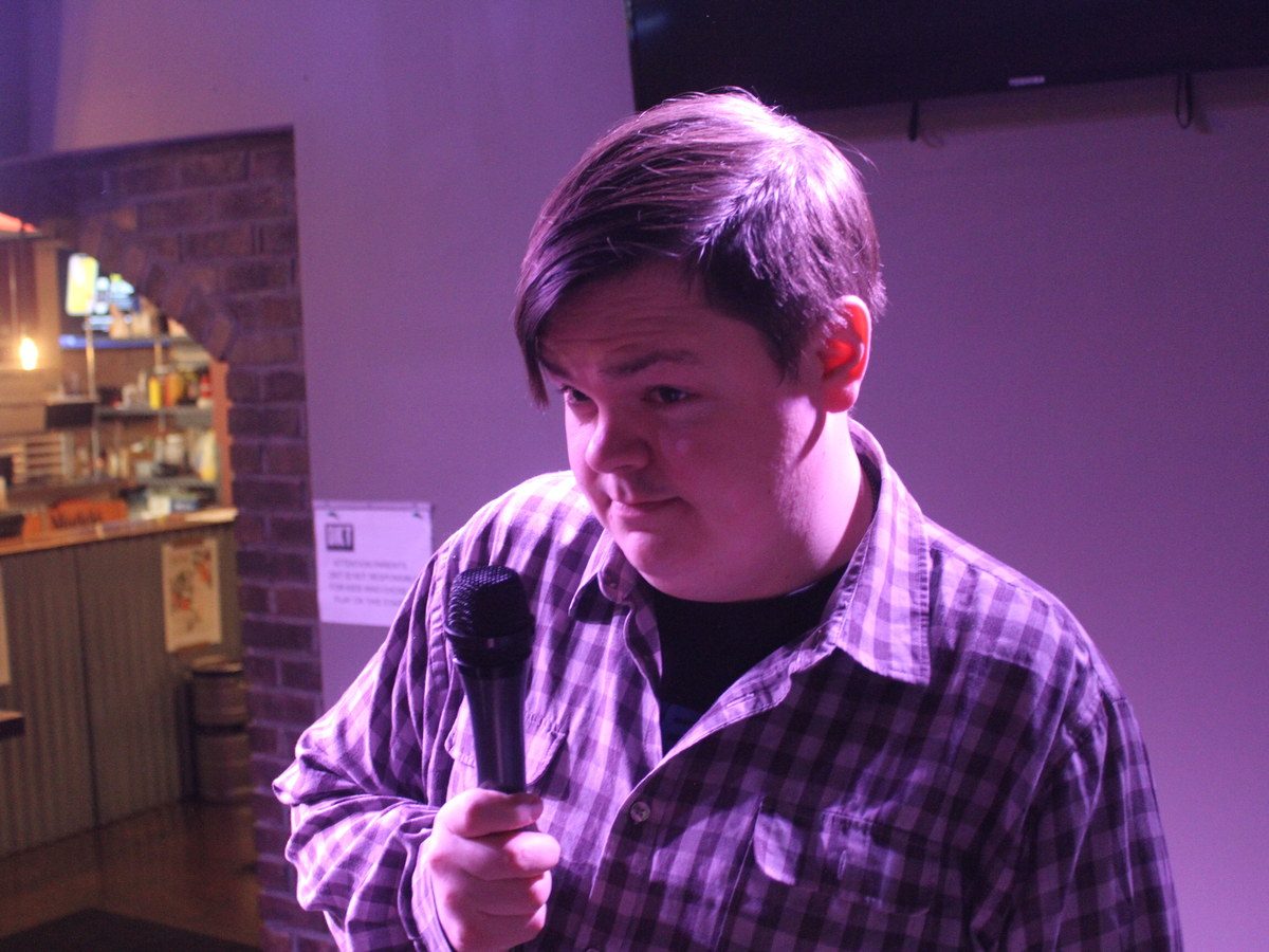 Comedian performing with a microphone under purple stage lighting