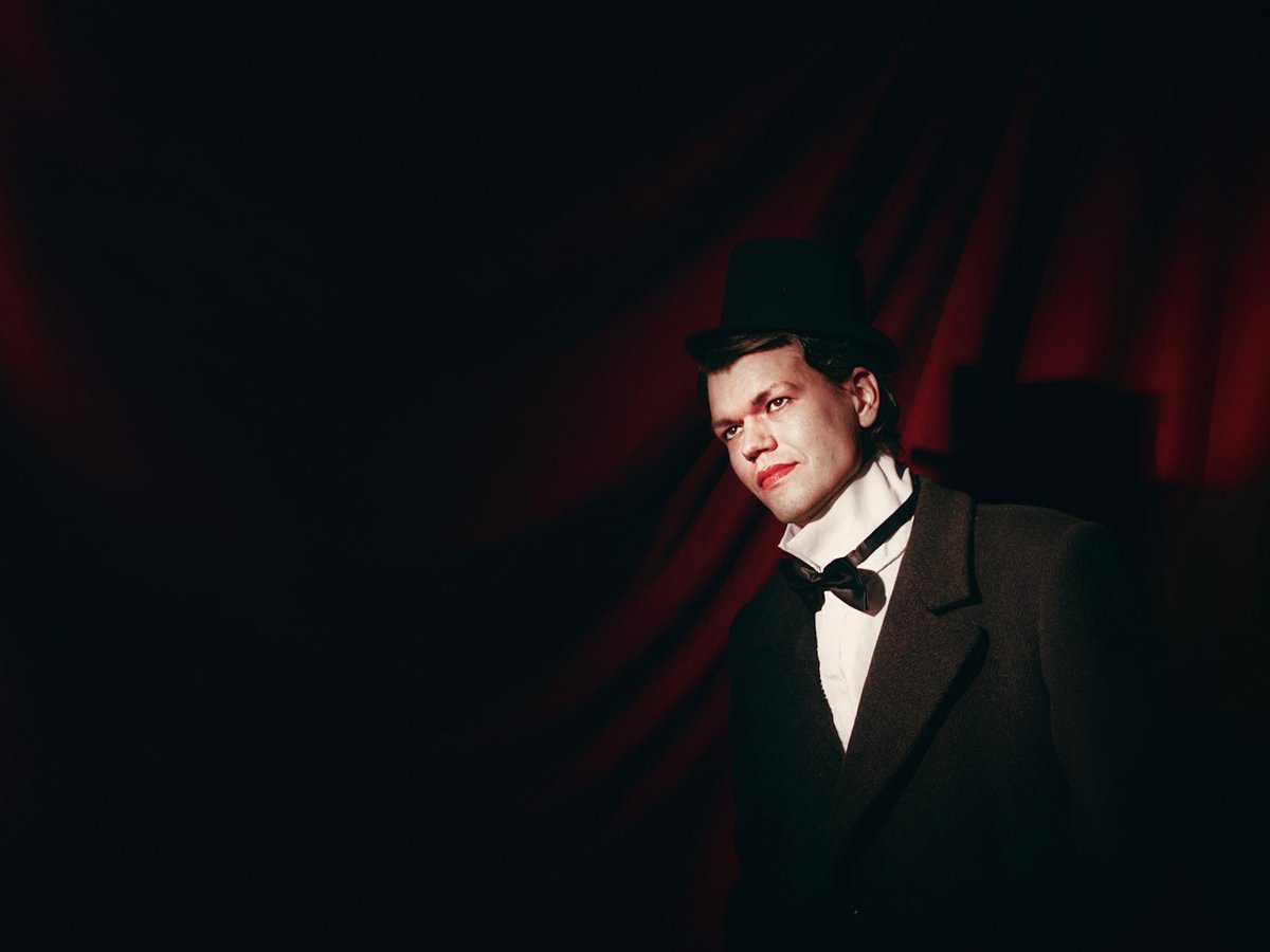 Magician in a tuxedo and top hat under a stage spotlight