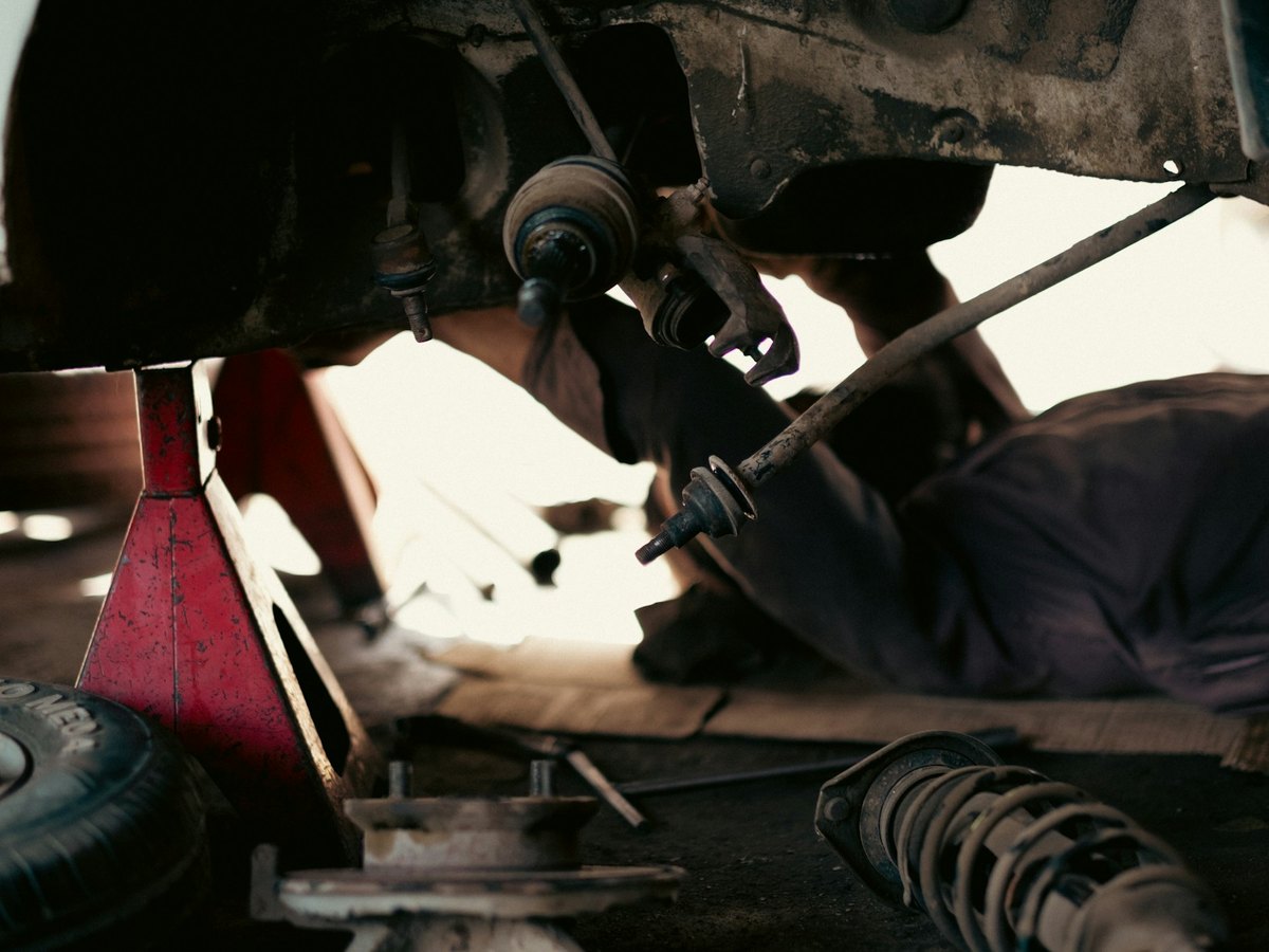 Mechanic inspecting suspension parts beneath a raised car