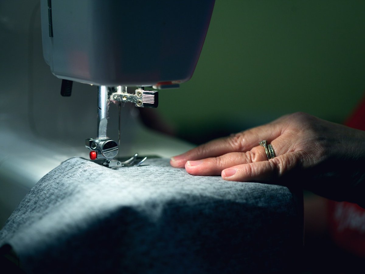 Tailor guiding gray fabric through a sewing machine